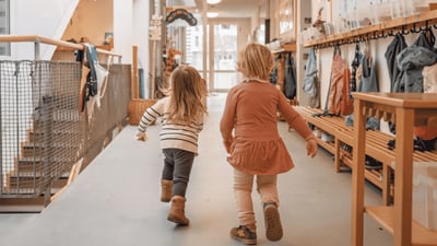 Zwei Kinder laufen gemeinsam durch den Flur einer Kindertagesstätte.