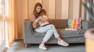 Mutter sitzt mit ihrem kleinen Kind auf dem Sofa und schaut auf ihr Smartphone.