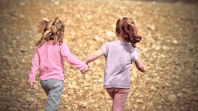Zwei Kinder laufen Hand in Hand über einen Spielplatz.