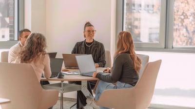 Vier Mitarbeitende der Little Bird Group sitzen mit Laptops an einem Besprechungstisch und tauschen sich in einem hellen Büro aus.