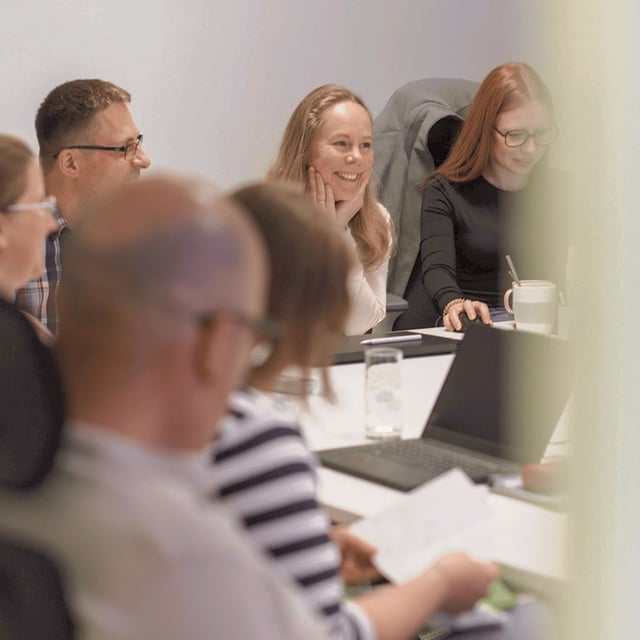 Mehrere Mitarbeitende der Little Bird Group sitzen gemeinsam in einer Besprechung, tauschen sich aus und lachen miteinander.