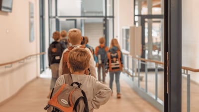 Mehrere Grundschulkinder mit Schulranzen laufen gemeinsam durch einen hellen Schulflur.