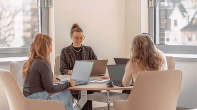 Drei Mitarbeiterinnen der Little Bird Group sitzen mit Laptops an einem Besprechungstisch und tauschen sich in einem hellen Büro aus.