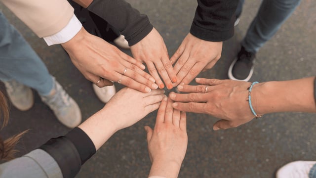 Mehrere Teammitglieder legen ihre Hände in der Mitte zusammen und symbolisieren damit Zusammenhalt und Zusammenarbeit.