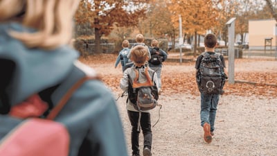 Mehrere Grundschulkinder mit Schulranzen laufen gemeinsam über einen herbstlichen Weg im Freien.