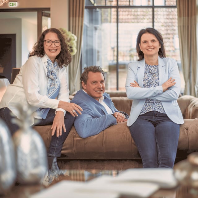 Drei Mitarbeitende des Vertriebsteams der Little Bird Group stehen und sitzen gemeinsam in einem hellen Besprechungsraum.