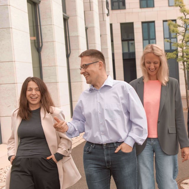 Drei Mitarbeitende der Little Bird Group gehen gemeinsam vor einem Bürogebäude entlang, unterhalten sich und lachen.