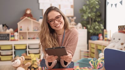 Einrichtungsleitung einer Kita sitzt in einem Gruppenraum und nutzt ein Tablet zur digitalen Organisation des Betreuungsalltags.